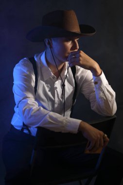 Klasik batı kovboy kıyafeti giymiş düşünceli bir çift cinsiyetli kadın modelin yan görüntüsü. Moody stüdyo portresi, mavi kenarlı aydınlatma ve puslu, dalgın bir şekilde başka yere bakıyor. Hikaye anlatma ve çeşitlilik için yüksek kalite kavramsal resim