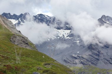 Electrical şanzıman kuleleri Stelvio Geçidi 'ndeki İtalyan Alpleri' nde karlı tepelerin ve alçak bulutların dramatik zeminine karşı duruyor. Modern altyapı ve vahşi dağ doğasının bir karışımı..