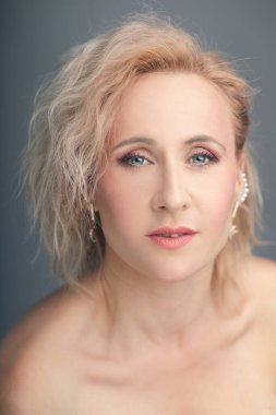 Kendine güvenen, orta yaşlı, sarı saçlı ve yumuşak makyajlı bir kadının yüksek kaliteli dikey portresi. Güzellik, cilt bakımı, yaşlanma karşıtı ve sağlıklı pazarlama kavramları için mükemmel.