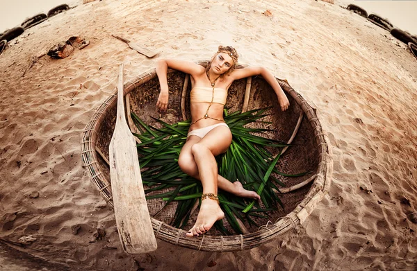 Hermosa joven rubia tumbada en la playa en un barco redondo Fotos de stock libres de derechos