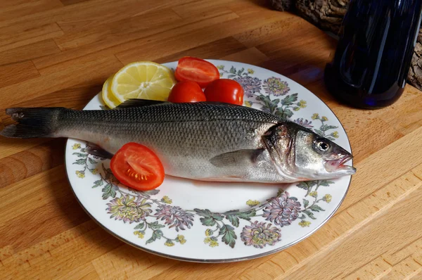 Lubina, spigola. Pescado fresco con la cabeza en el plato . — Foto de Stock