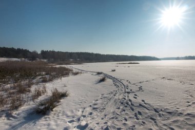Güneşli bir kış gününde karla kaplı bir gölün üzerindeki buz kabuğu.