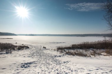 Güneşli bir kış gününde karla kaplı bir gölün üzerindeki buz kabuğu.