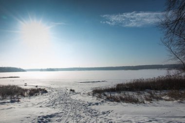 Güneşli bir kış gününde karla kaplı bir gölün üzerindeki buz kabuğu.