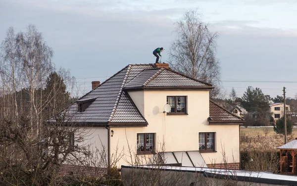 A chimney sweep cleans the chimney on the roof of a detached house in winter