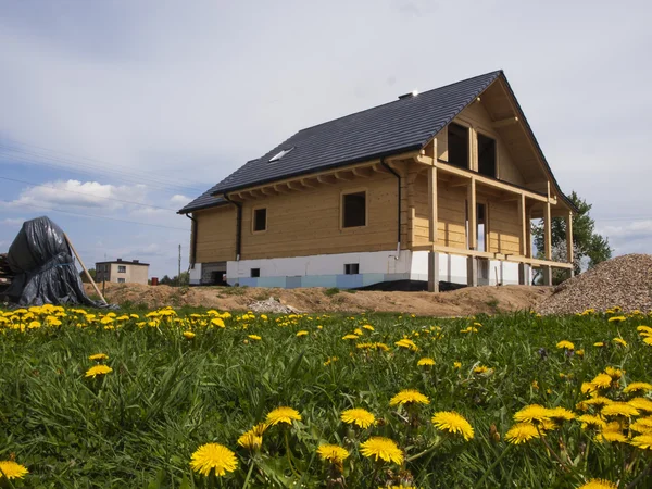 Costruzione di una casa in legno e denti di leone gialli nel prato — Foto Stock