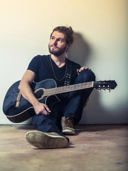 Joven sentado y sosteniendo la guitarra — Foto de Stock