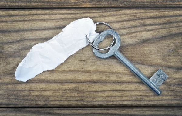 Key with empty note on wooden table — Stock Photo, Image