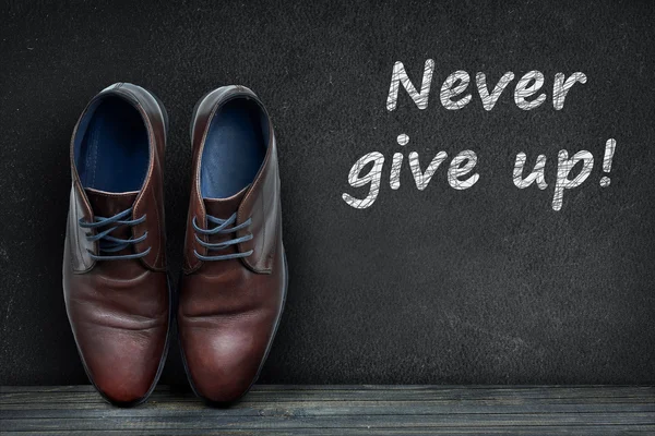 Never give up text on black board and business shoes