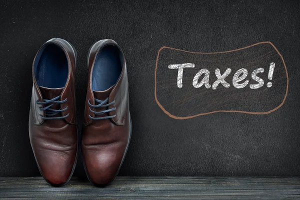 Taxes text on black board and business shoes — Stock Photo, Image