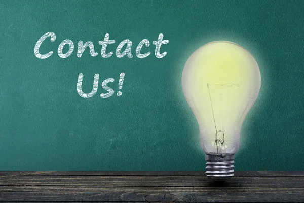 Contact Us text and light bulb on table — Stock Photo, Image