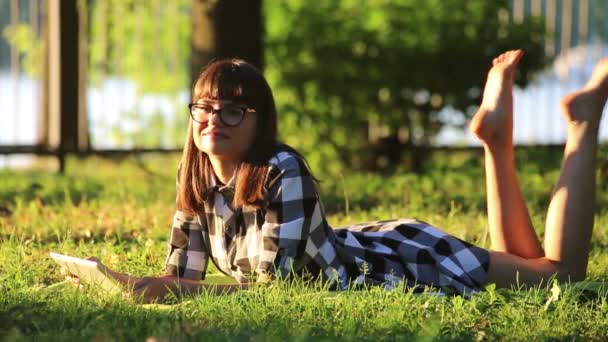 Chica es relajarse en el parque con una tableta PC — Vídeo de stock