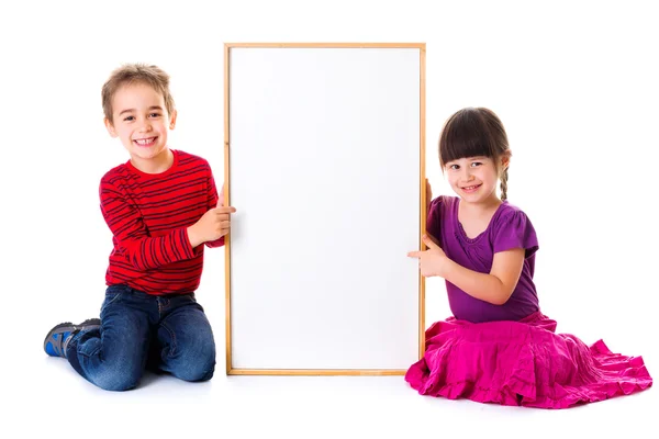 Niedliche Mädchen und Jungen sitzen in der Nähe leere Anzeige — Stockfoto