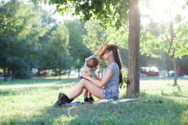 Anne ve yaz tatili ağacın altında oturup yürümeye başlayan çocuk