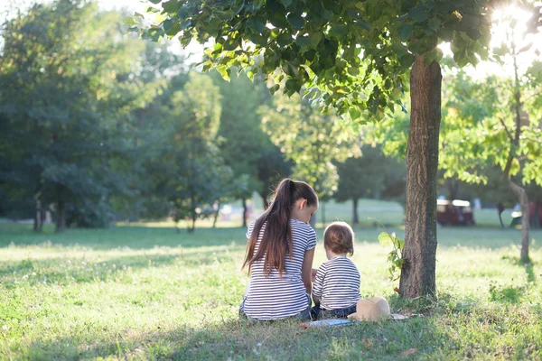 Moeder en peuter zitten onder de boom tijdens de zomervakantie — Stockfoto