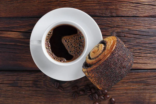 Cup of coffee and bun with poppy seeds on wooden background, top view
