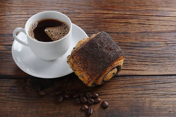 Cup of coffee and bun with poppy seeds on wooden background