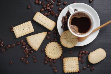 Çeşitli kurabiyeler ve bir fincan kahve. Siyah ahşap masa, üst manzara.