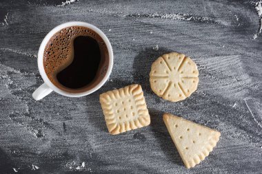 Çeşitli kurabiyeler ve bir fincan kahve, siyah masa üzerinde un, üst manzara.