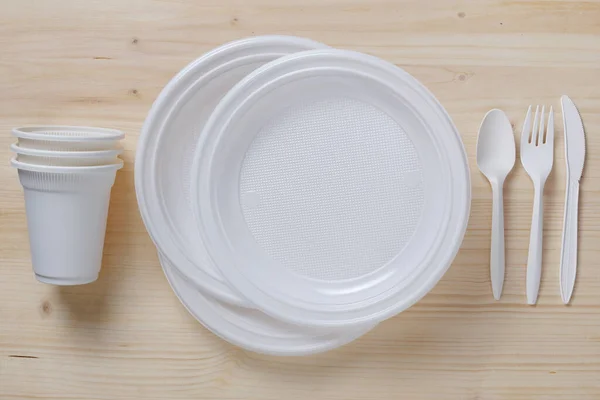 Disposable tableware and cutlery on wooden background, top view