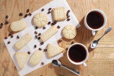 Eski ahşap masada iki fincan kahve ve çeşitli kurabiyeler.