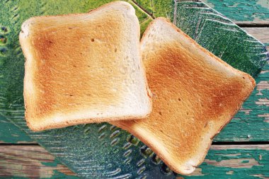 Eski yeşil ahşap masada, seramik tahtada iki dilim tost. Yaklaş, üst manzara.