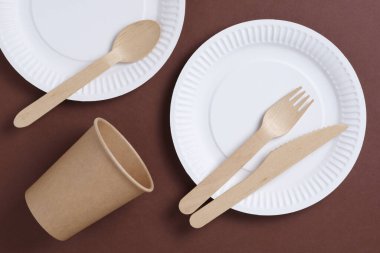 Kahverengi karton zemin üzerinde ahşap ve kağıttan yapılmış tek kullanımlık sofra takımı.