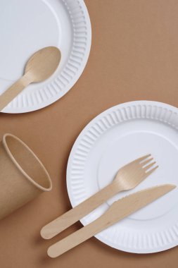 Kahverengi karton zemin üzerinde ahşap ve kağıttan yapılmış tek kullanımlık sofra takımı.