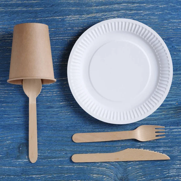 Tek kullanımlık sofra takımı ve ahşap ve kağıttan yapılmış çatal bıçak takımı mavi bir masanın üstünde.