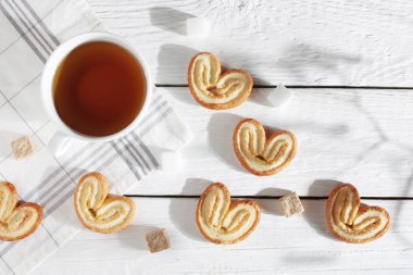 Kalp şeklinde poğaça kurabiyeleri ve beyaz ahşap bir masada bir fincan çay.