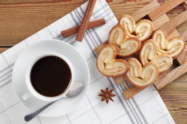 Kalp şeklinde poğaça kurabiyeleri ve ahşap masada bir fincan kahve.