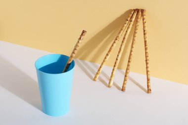 Mavi plastik bardakta susam tohumlu pipetler ve beyaz-sarı arka planda