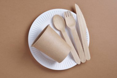 Kahverengi karton zemin üzerinde ahşap ve kağıttan yapılmış tek kullanımlık sofra takımı.