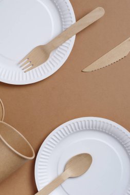 Kahverengi karton zemin üzerinde ahşap ve kağıttan yapılmış tek kullanımlık sofra takımı ve çatal bıçak takımı.