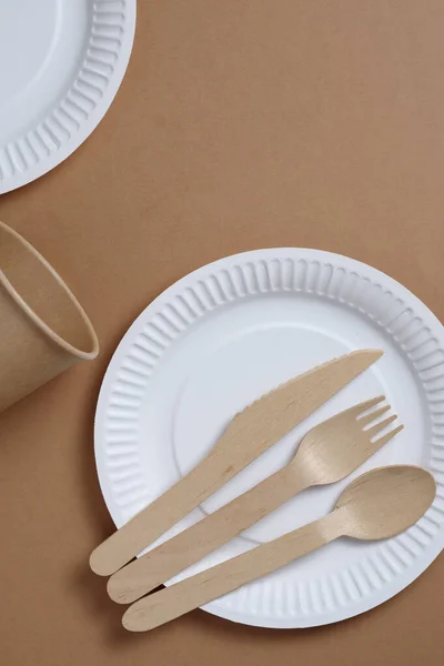 Disposable tableware and cutlery made of wood and paper on a brown cardboard background, top view
