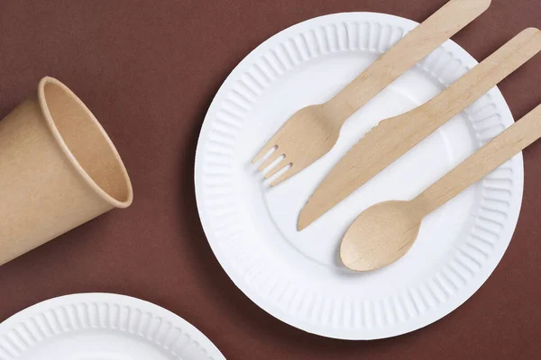 Disposable tableware and cutlery made of wood and paper on a brown cardboard background, top view