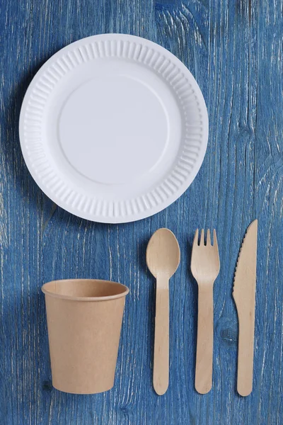 Disposable eco-friendly tableware made of wood and paper on a blue table, top view