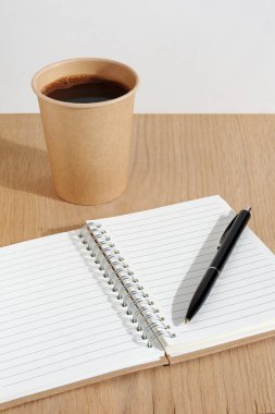 Not defteri, kalem ve tek kullanımlık kahve bardağı masanın üstünde.