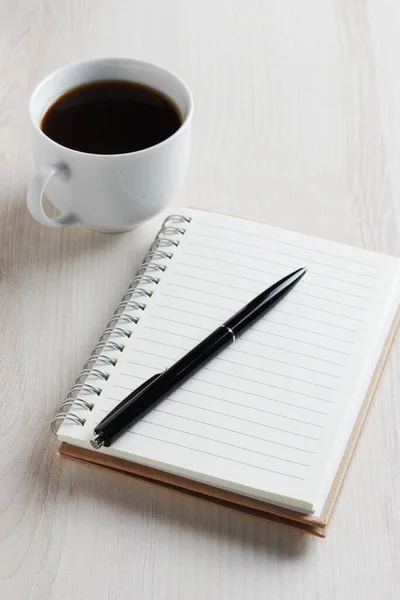 Notepad and pen with a cup of black coffee on light table close up