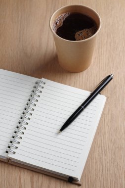 Spiral defter, kalem ve tek kullanımlık kahve bardağı masanın üstünde.