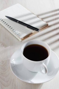 Bir fincan sade kahve ve kalem ile ışıklı masaya yakın.