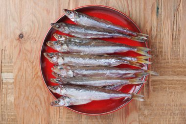 Eski ahşap arka planda kırmızı tabakta tuzlanmış kapelinli balık. 