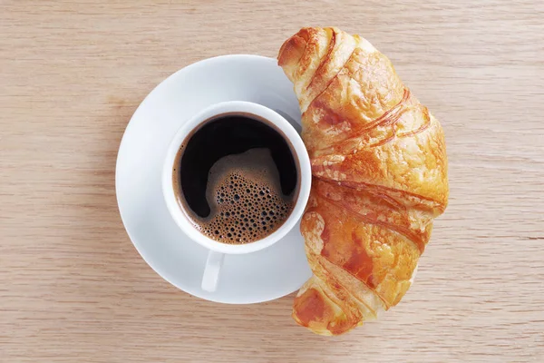 Freshly baked croissant and coffee for breakfast on wooden background or table, top view