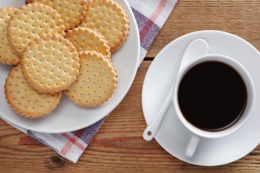 Kremalı kurabiyeler tabakta ve bir fincan kahve masanın üstünde.