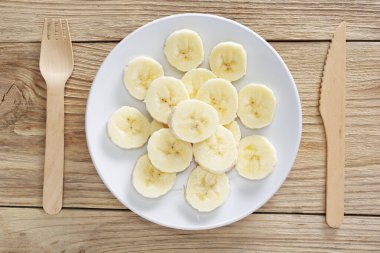 Taze taze kesilmiş muzlar bir tabakta ve ahşap çatal bıçak seti sarı arka planda, üst manzara