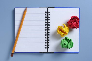 Renkli kağıt topların yüksek açılı görünümü ve mavi masadaki kalemli defter