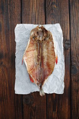 Salted dried fish on crumpled paper located on wooden table, top view