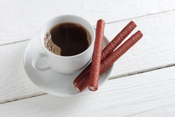Cup of coffee and chocolate wafer sticks on white wooden background