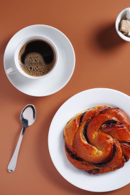 Kahverengi arka planda kahvaltı için çörek ve bir fincan kahve.