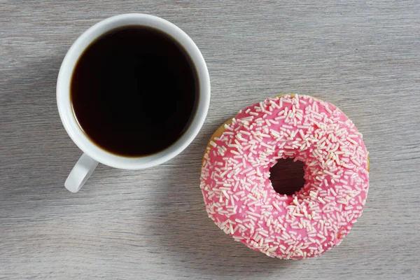 桌上放着一杯热咖啡和粉红的甜甜圈 上面有洒水 — 图库照片